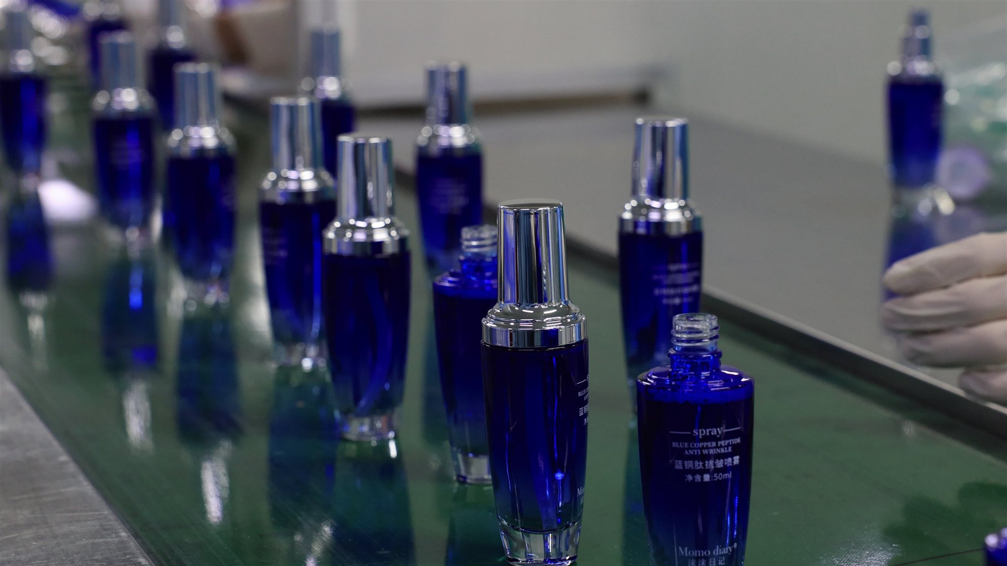 Blue glass skincare bottles moving along a filling line at the jogonglabs factory
