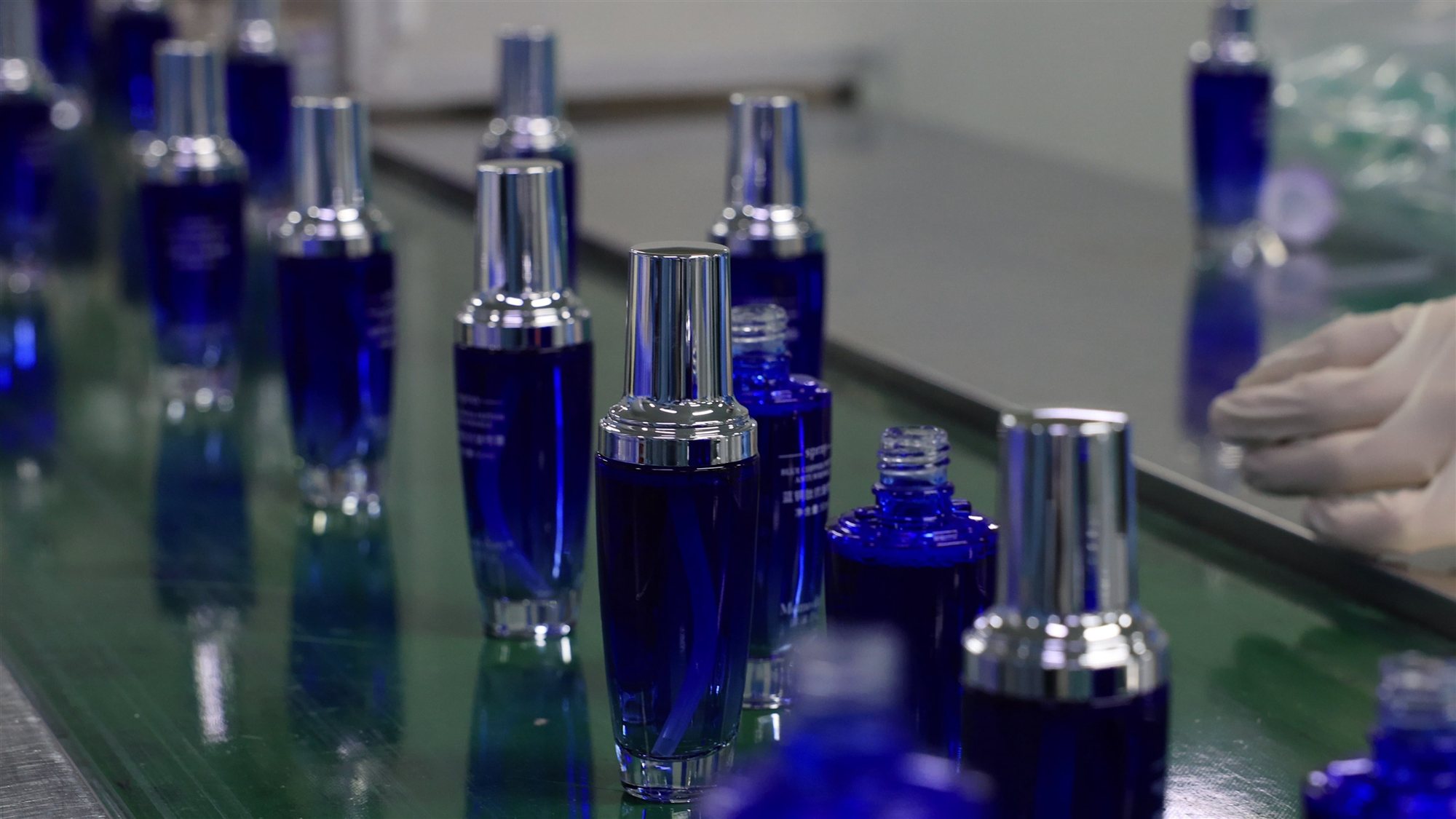 Blue glass skincare bottles moving along a filling line at the jogonglabs factory