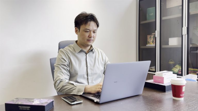 Tyler, founder of jogonglabs, comparing documents at his desk in the Guangzhou office